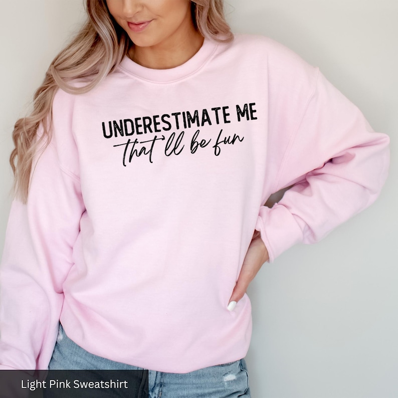 a woman wearing a pink sweatshirt that says, underestimate me that '