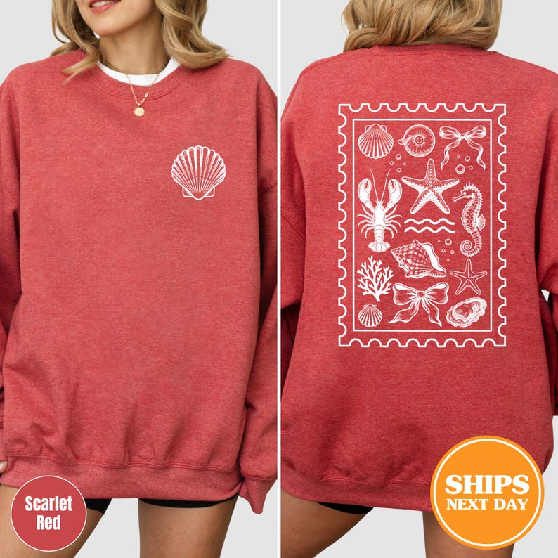May include: A scarlet red crewneck sweatshirt featuring a white line art graphic of a single seashell on the left chest. The back displays a large rectangular stamp-shaped design containing white line illustrations of various sea life.