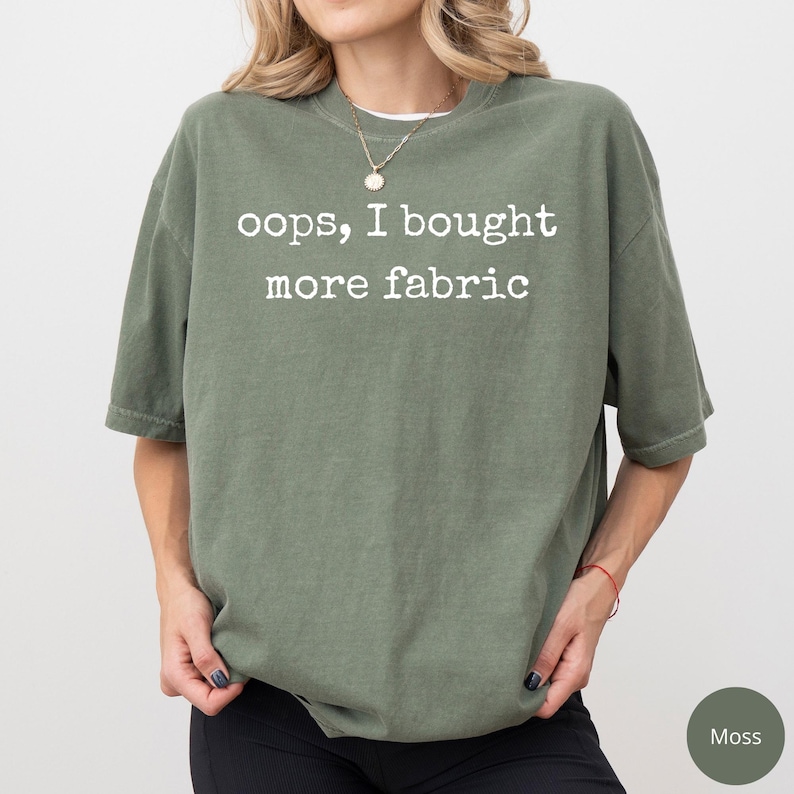 A woman wearing a green t-shirt with the text "oops, I bought more fabric" printed on it.