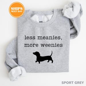 A gray sweatshirt with a black silhouette of a dachshund dog and the text "less meanies, more weenies" printed on it.