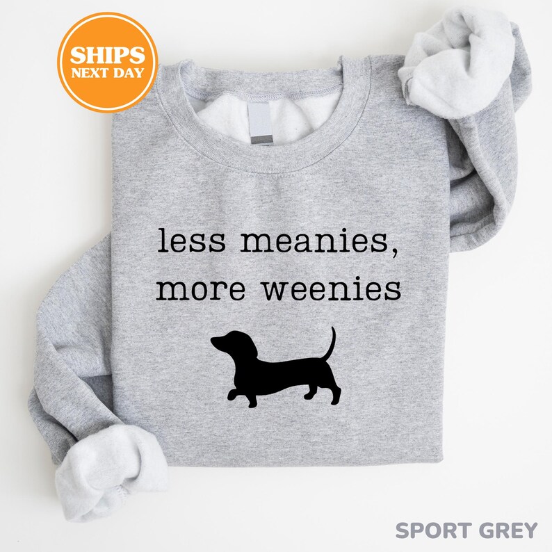 A gray sweatshirt with a black silhouette of a dachshund dog and the text "less meanies, more weenies" printed on it.