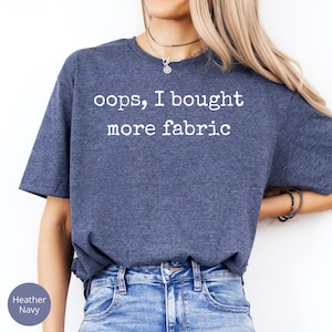 A woman wearing a blue t-shirt with the text "oops, I bought more fabric" printed on it.