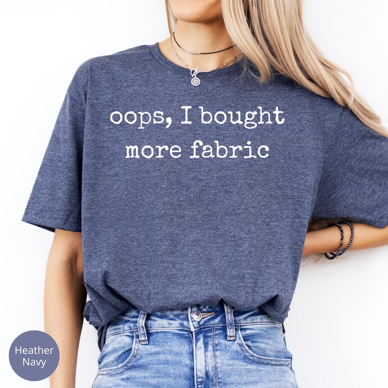 A woman wearing a blue t-shirt with the text "oops, I bought more fabric" printed on it.