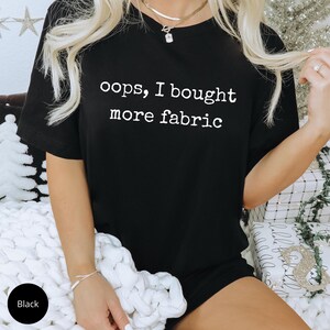 A person wearing a black t-shirt with the text "oops, I bought more fabric" printed on it.