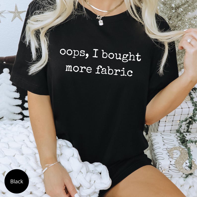 A person wearing a black t-shirt with the text "oops, I bought more fabric" printed on it.
