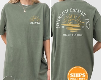 May include: A moss green short-sleeve t-shirt featuring a small yellow sun graphic and the name OLIVIA on the front left chest. The back displays a large yellow sun graphic with the text JOHNSON FAMILY TRIP, 2026, and MIAMI, FLORIDA.