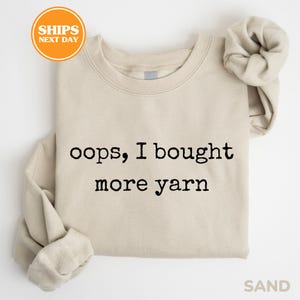 A beige t-shirt with the text "oops, I bought more yarn" printed on it.