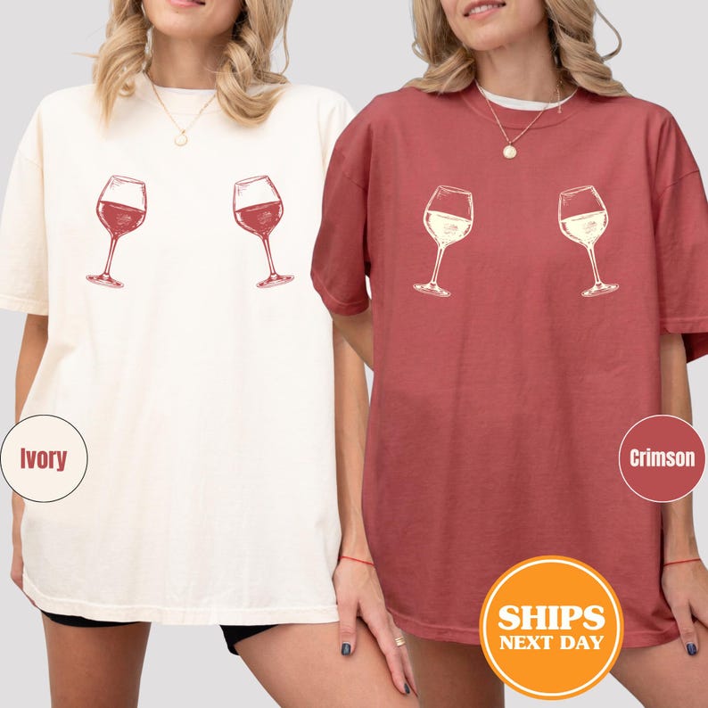 May include: Two t-shirts, one ivory and one crimson, each featuring a graphic of two wine glasses. The ivory shirt has red wine glasses, while the crimson shirt has white wine glasses. The shirts are casual and comfortable.