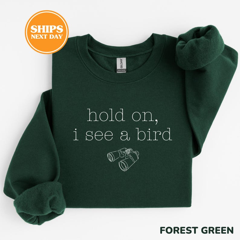 A green sweatshirt with the text "hold on, I see a bird" printed on it, along with a small illustration of binoculars.