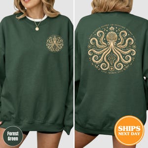 Puede incluir: Sudadera verde bosque con un dise&ntilde;o de pulpo dorado en la parte delantera y trasera. El dise&ntilde;o trasero incluye el texto "When injustice becomes law, resistance becomes duty" y "Love Trumps Hate".