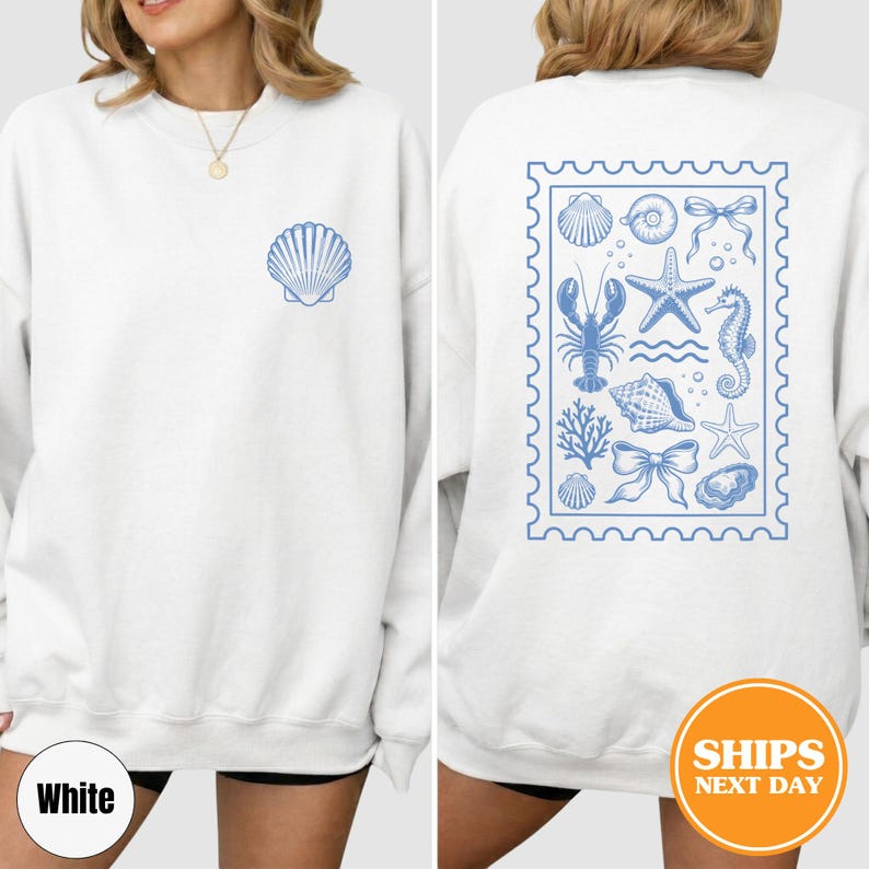 May include: A white crewneck sweatshirt featuring a small blue seashell graphic on the front left chest. The back displays a large rectangular postage stamp design filled with blue illustrations of sea life, including a lobster, starfish, and seahorse.