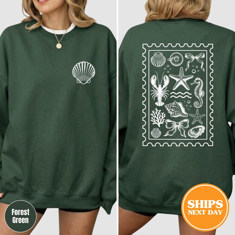 May include: A forest green crewneck sweatshirt featuring a white shell graphic on the left chest. The back displays a large white rectangular stamp-shaped design containing illustrations of a lobster, starfish, seahorse, shells, and bows.