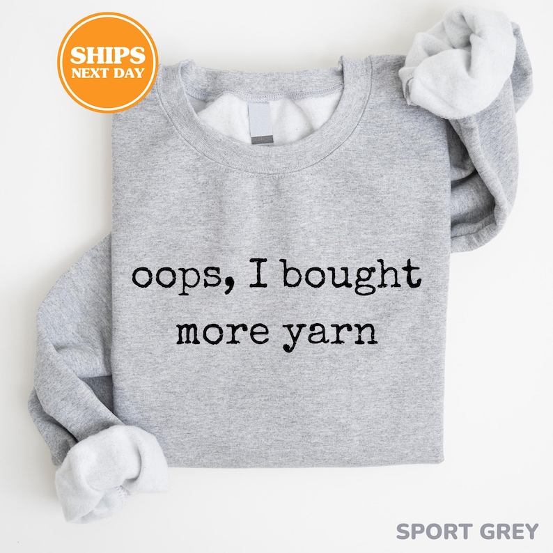 A gray sweatshirt with the text "oops, I bought more yarn" printed on it.