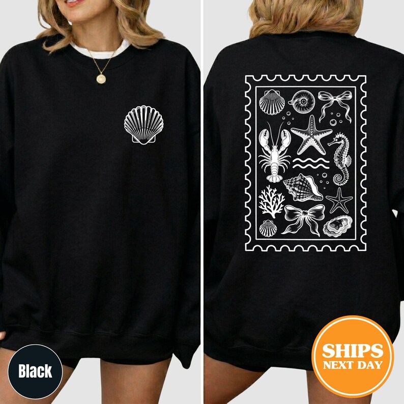May include: A black long-sleeve sweatshirt featuring a white graphic of a single seashell on the front left chest. The back displays a large white rectangular stamp-shaped design containing illustrations of a lobster, starfish, and shells.