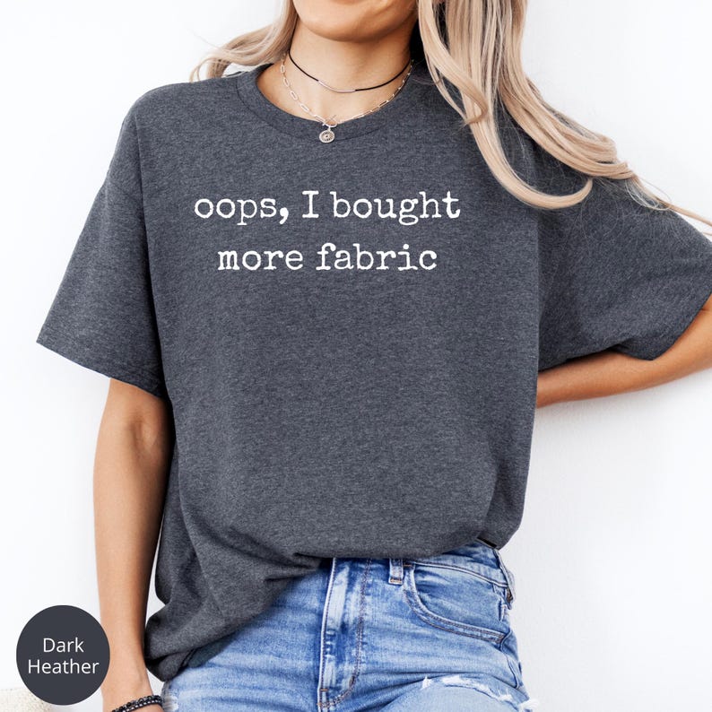 A woman wearing a gray t-shirt with the text "oops, I bought more fabric" printed on it.