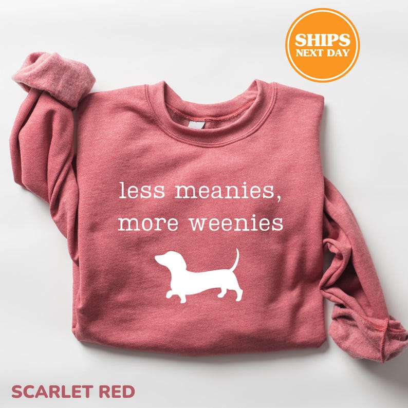 A red sweatshirt with the text "less meanies, more weenies" printed on it, along with a white silhouette of a dog.