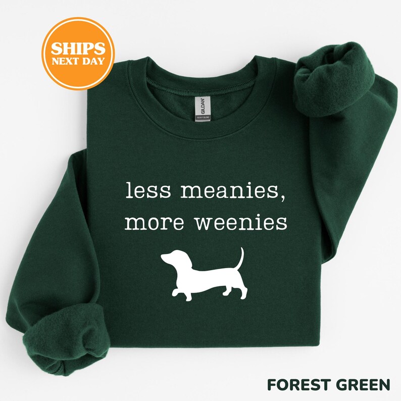 A green sweatshirt with the text "less meanies, more weenies" printed on it, along with a white silhouette of a dog.