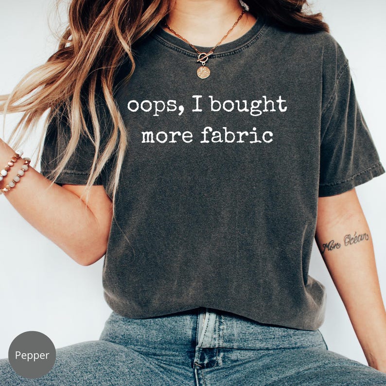 A person wearing a gray t-shirt with the text "oops, I bought more fabric" printed on it.