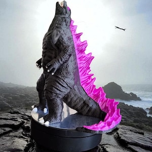 Pode incluir: Uma figura de monstro preta com uma superfície texturizada e escamosa e barbatanas dorsais rosa brilhante ao longo das costas. A criatura tem garras brancas nas mãos e nos pés, e a boca aberta voltada para cima sobre uma base circular.