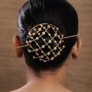 May include: A gold-toned metal hair bun cage featuring a lattice design with small flower accents at each intersection. Each flower centre is adorned with a tiny white pearl. A long, slender gold-toned hair stick secures the cage through the hair bun.