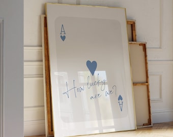 May include: A framed art print featuring a playing card design with the Ace of Hearts. The print has a gold frame and the text "How lucky are we?" in a handwritten font. The artwork is displayed against a white wall.