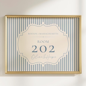 May include: A rectangular wall sign in a gold frame featuring a blue and white vertical striped background. A central cream-colored label shape displays the text BOSTON • MASSACHUSETTS, ROOM 202, and the names Olivia & Harper in blue lettering.