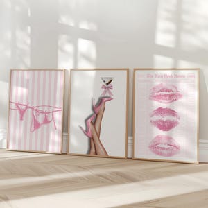 May include: Three framed art prints. The first features pink striped background with pink lingerie hanging on a clothesline. The second shows legs in pink high heels holding a martini glass. The third print displays three pink lip imprints.