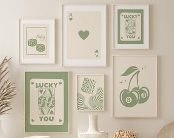 May include: A set of six green and cream framed prints with various designs. The prints feature a playing card, dice, cherries, a queen of hearts, and a wavy design. The prints are hung on a white wall above a white bench with two wicker baskets.