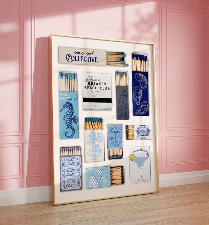May include: A white frame filled with matchboxes featuring various designs, including a seashell, a surfboard, an oyster, and a cocktail glass. The matchboxes are labeled with text such as "Sun & Surf Collective", "Breaker Beach Club", "East Coast", and "The Cocktail Club".