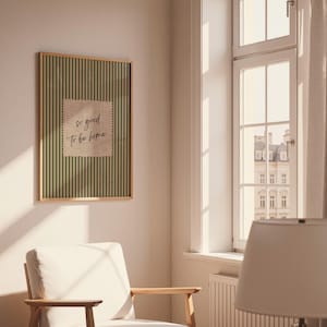 May include: A framed wall art print with a gold-colored frame. The artwork features a green striped background with a beige square in the center. The text "so good to be home" is written in a handwritten style on the beige square.
