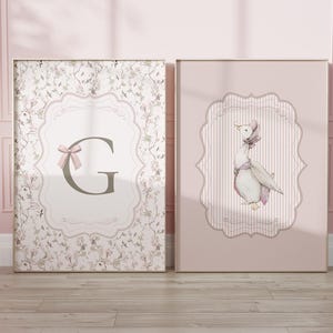 May include: Two framed art prints. One features a floral pattern with a letter "G" and a pink bow. The other print shows a watercolor illustration of a goose wearing a bonnet, set against a pink striped background.