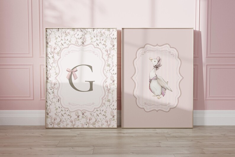May include: Two framed art prints. One features a floral pattern with a letter "G" and a pink bow. The other print shows a watercolor illustration of a goose wearing a bonnet, set against a pink striped background.