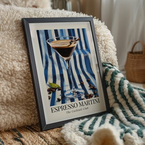 May include: A framed print of an espresso martini cocktail in a martini glass on a blue and white striped background with coffee beans scattered around the glass. The text "Espresso Martini" and "The Cocktail Club" is printed below the glass.