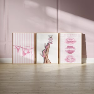 May include: Three framed art prints with a pink theme. One print shows pink lingerie hanging on a clothesline. Another features legs in pink heels holding a martini. The third displays pink lip prints.