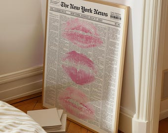 Può includere: Stampa incorniciata di una pagina di giornale con tre impronte di baci di rossetto rosa. Il giornale è intitolato "The New York News" e datato 27 luglio 2025. La cornice è di colore legno chiaro.