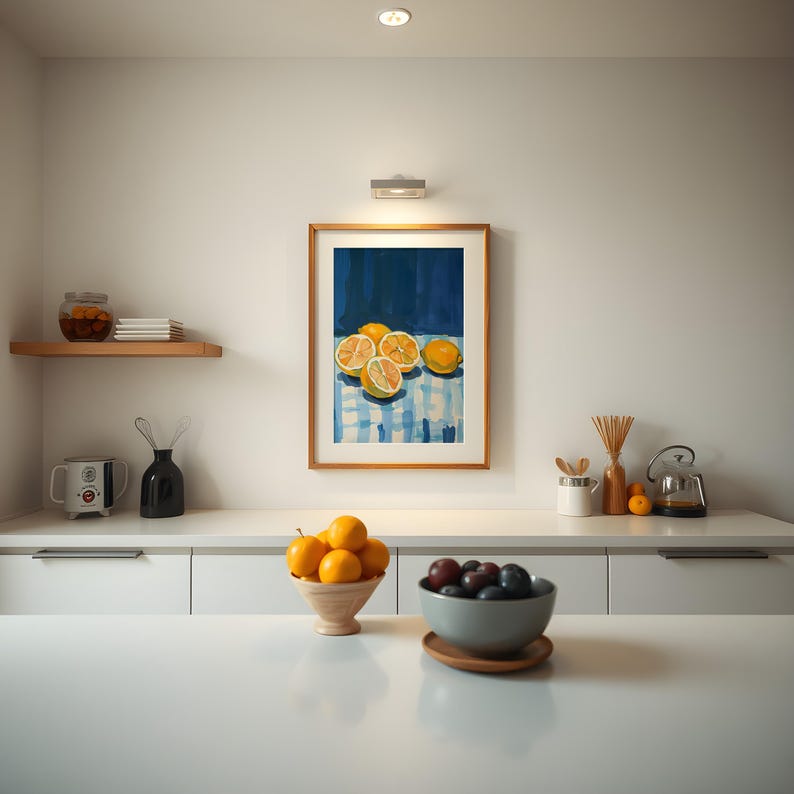 May include: A framed painting of lemons on a blue and white checkered tablecloth. The painting is hanging on a white wall above a white countertop with a bowl of lemons and a bowl of plums.
