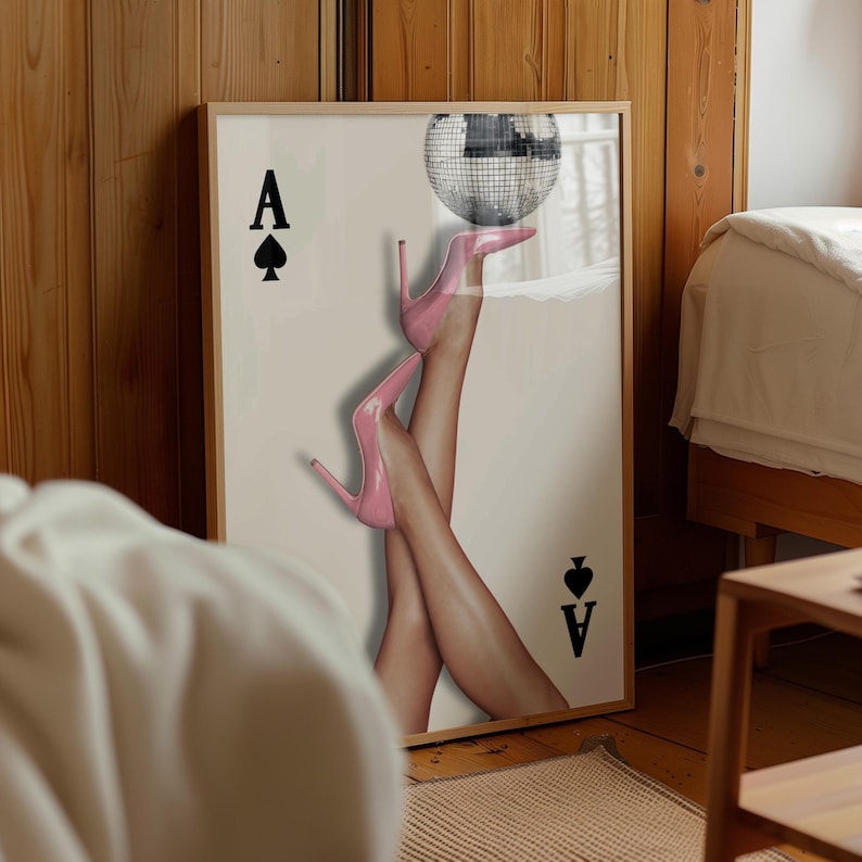 May include: Framed art print showing legs in pink high heels balancing a disco ball. The print includes the Ace of Spades card symbol and text. The artwork is displayed in a room with wooden paneling.