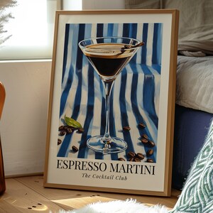 May include: A framed poster with a blue and white striped background featuring a martini glass filled with a dark brown liquid. The glass has a cinnamon stick garnish. The text "Espresso Martini The Cocktail Club" is printed below the glass.