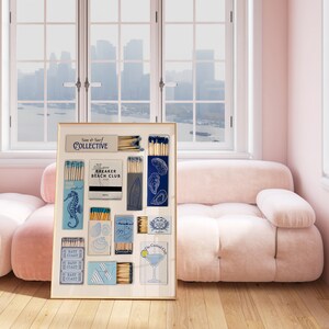 May include: A framed collage of vintage matchboxes with nautical themes, including a seahorse, an oyster, a sailboat, and a cocktail. The matchboxes are arranged in a grid pattern on a white background. The frame is gold and has a white mat. The text "Sun & Surf Collective" is visible on one of the matchboxes.