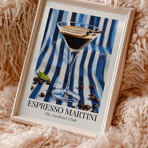 May include: A framed print of a cocktail called an Espresso Martini. The drink is in a martini glass on a blue and white striped background with coffee beans scattered around it. The text "Espresso Martini" and "The Cocktail Club" is printed below the glass.