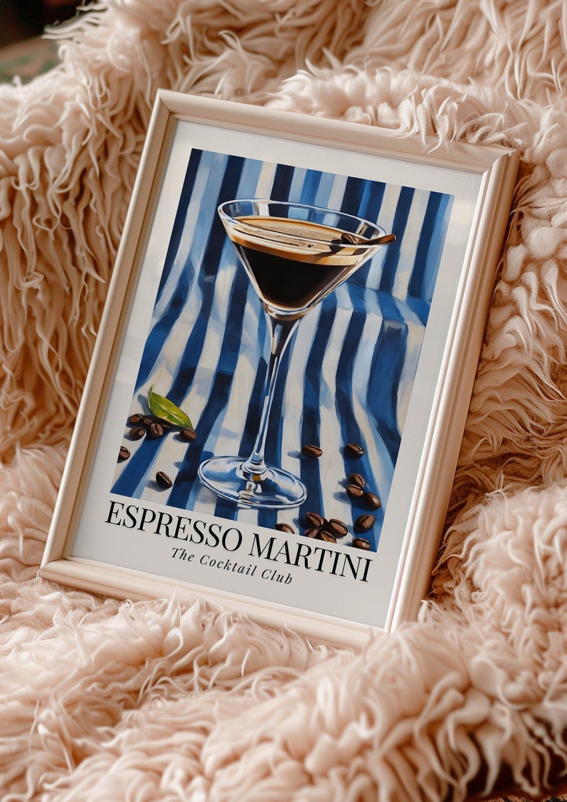 May include: A framed print of a cocktail called an Espresso Martini. The drink is in a martini glass on a blue and white striped background with coffee beans scattered around it. The text "Espresso Martini" and "The Cocktail Club" is printed below the glass.