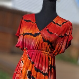 Pode incluir: Um vestido maxi tie-dye vermelho, laranja e preto com decote em V e mangas curtas. O vestido tem um corpete justo e uma saia fluida.