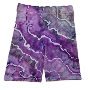 May include: Purple tie-dye cycling shorts with white stitching. The shorts display a marbled pattern in shades of purple, lavender, and grey. The fabric has a soft, textured appearance. The shorts are designed to be form-fitting.