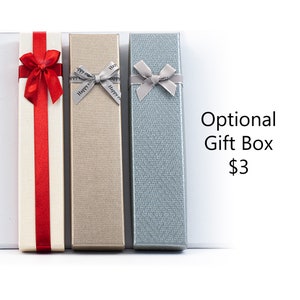 Op de afbeelding: Drie cadeaudozen met verschillende gekleurde linten. De dozen zijn wit, goud en blauw. De tekst "Optionele cadeaudoos € 3" is zichtbaar in de afbeelding.