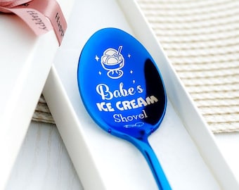 May include: A shiny blue ice cream shovel with the text "Babe's ICE CREAM Shovel" and an ice cream sundae graphic. The spoon is in a white gift box with a pink ribbon.