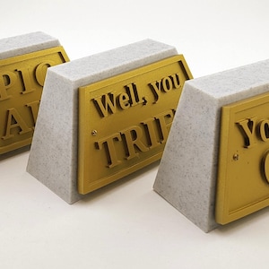 May include: Three small, triangular, gray concrete bases with gold plaques. The plaques have the following text: "Epic Fail", "Well, you tried", and "You did OK".