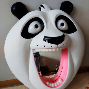 Puede incluir: Una gran cabeza de oso panda blanco con orejas y marcas oculares negras. El panda tiene la boca muy abierta con el interior rosa, revelando dientes blancos. Los ojos son azules. Este art&iacute;culo decorativo es probablemente un colgante de pared o un espejo.