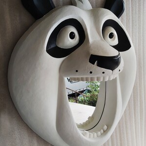 Puede incluir: Un espejo blanco con forma de oso panda con detalles negros alrededor de los ojos y las orejas. El espejo tiene un dise&ntilde;o de boca abierta, creando una est&eacute;tica &uacute;nica y juguetona. El espejo es una decoraci&oacute;n de pared.