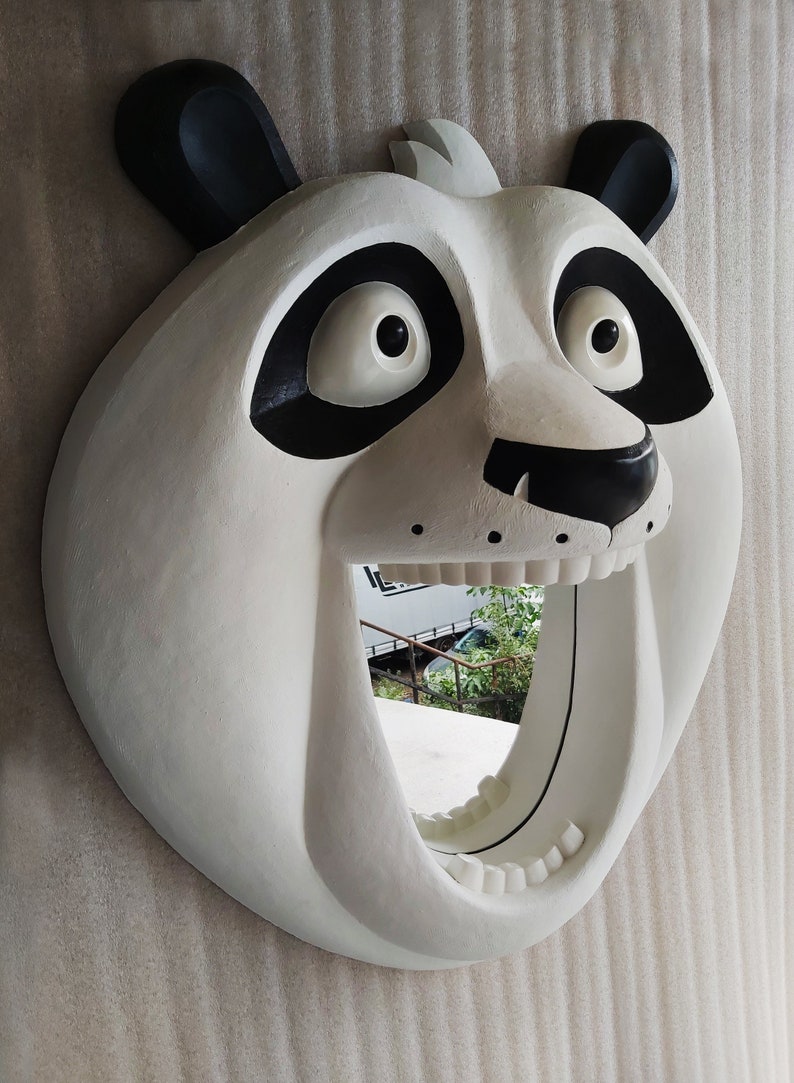 Puede incluir: Un espejo blanco con forma de oso panda con detalles negros alrededor de los ojos y las orejas. El espejo tiene un dise&ntilde;o de boca abierta, creando una est&eacute;tica &uacute;nica y juguetona. El espejo es una decoraci&oacute;n de pared.
