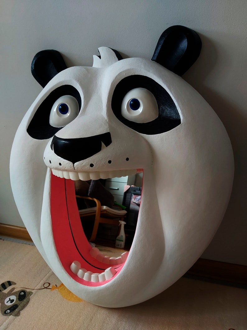 Puede incluir: Un gran espejo blanco con forma de oso panda con detalles negros alrededor de los ojos y las orejas. La boca del panda est&aacute; abierta, revelando un interior rosa y dientes. El espejo refleja la habitaci&oacute;n.